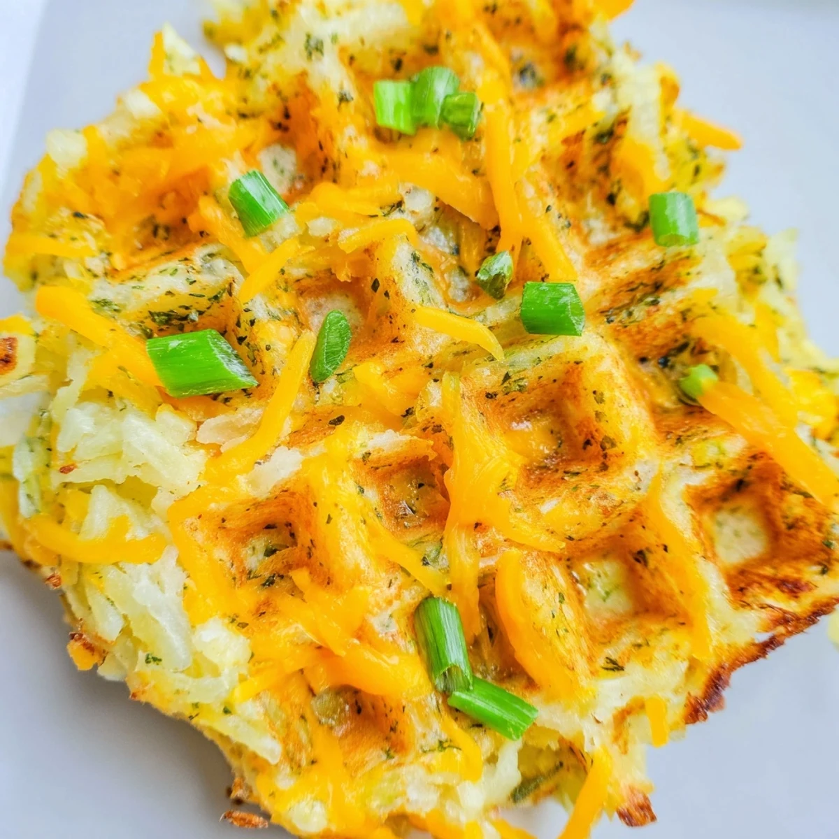 A close-up of crispy, flavorful Cheesy Hash Brown Waffles, studded with melted cheddar cheese.