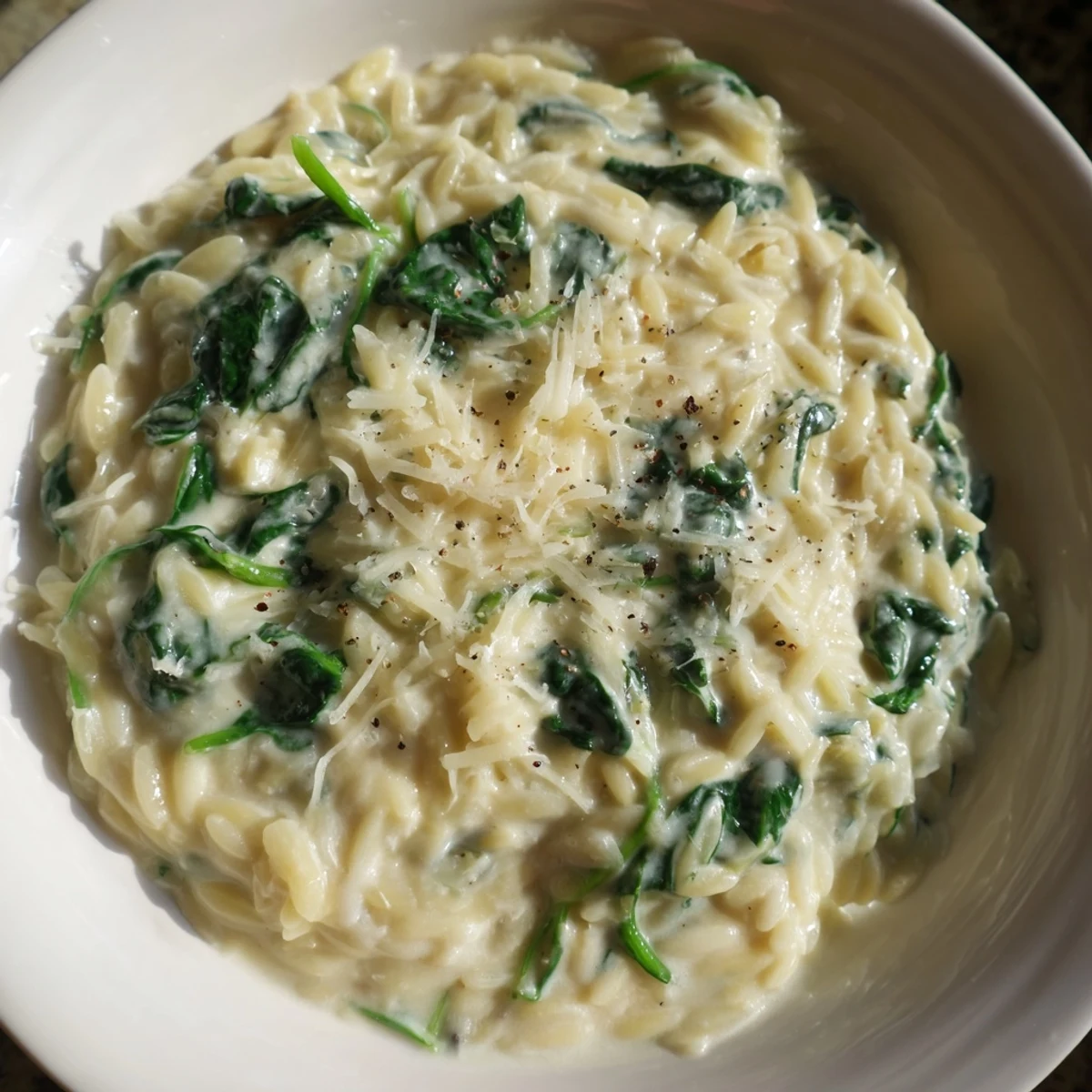 Close-up of bubbling creamy spinach orzo, dotted with fresh green spinach and Parmesan.