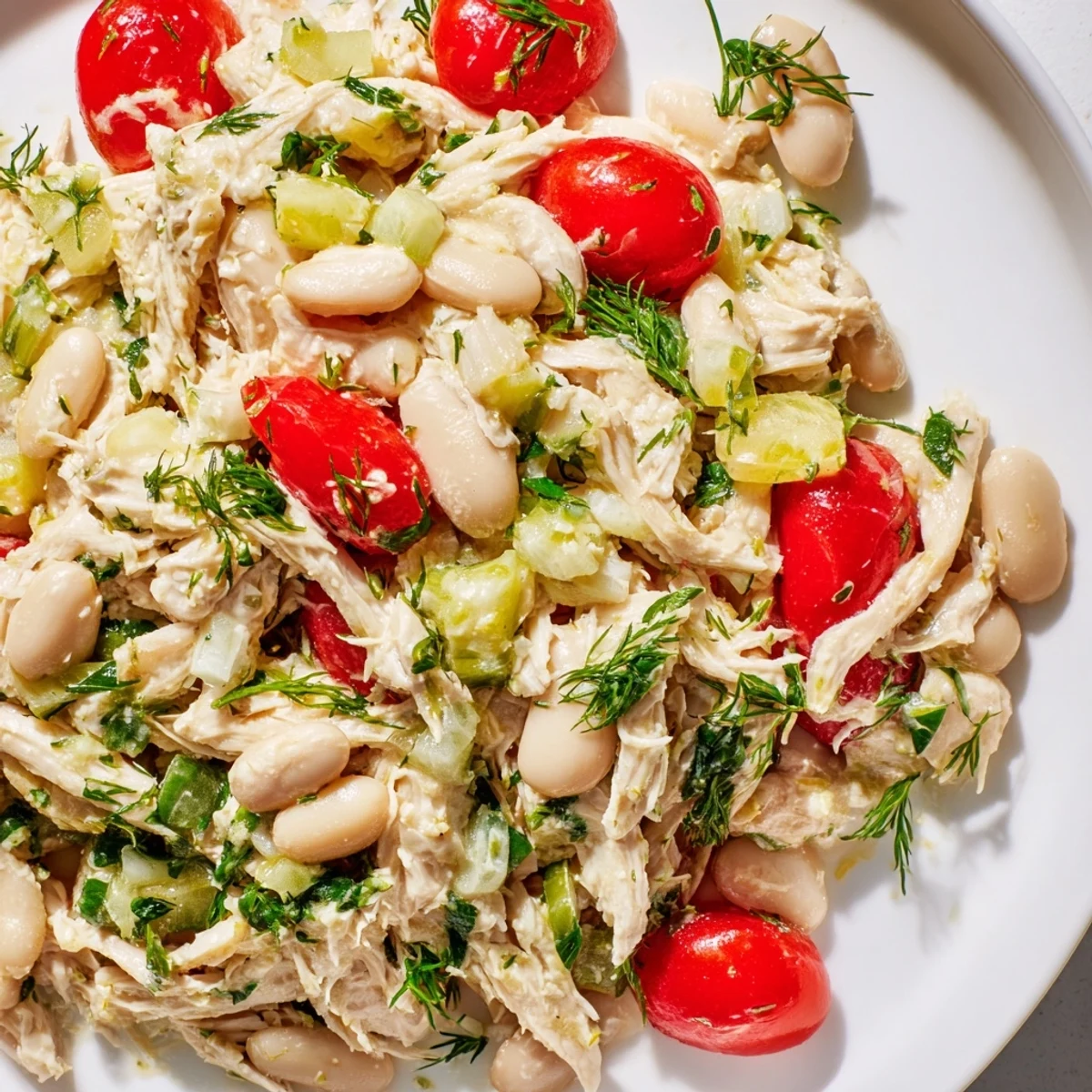 Vibrant Lemony White Bean Chicken Salad served in a white bowl, featuring tender shredded chicken, creamy white beans, diced celery, and fresh herbs glistening with a tangy lemon vinaigrette.