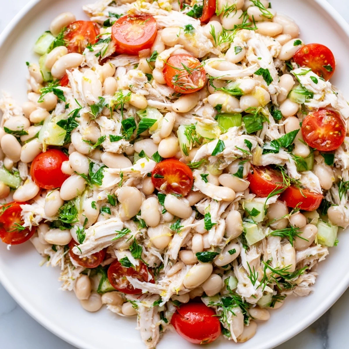 A refreshing Lemony White Bean Chicken Salad garnished with dill, arranged on a rustic plate with lemon wedges, perfect for a light gluten-free lunch or main dish.