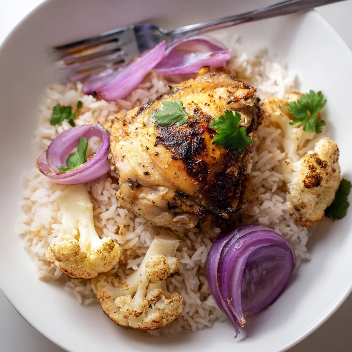 Golden-brown roasted cauliflower chicken sheet pan served over fluffy basmati rice, garnished with fresh parsley and lemon wedges.