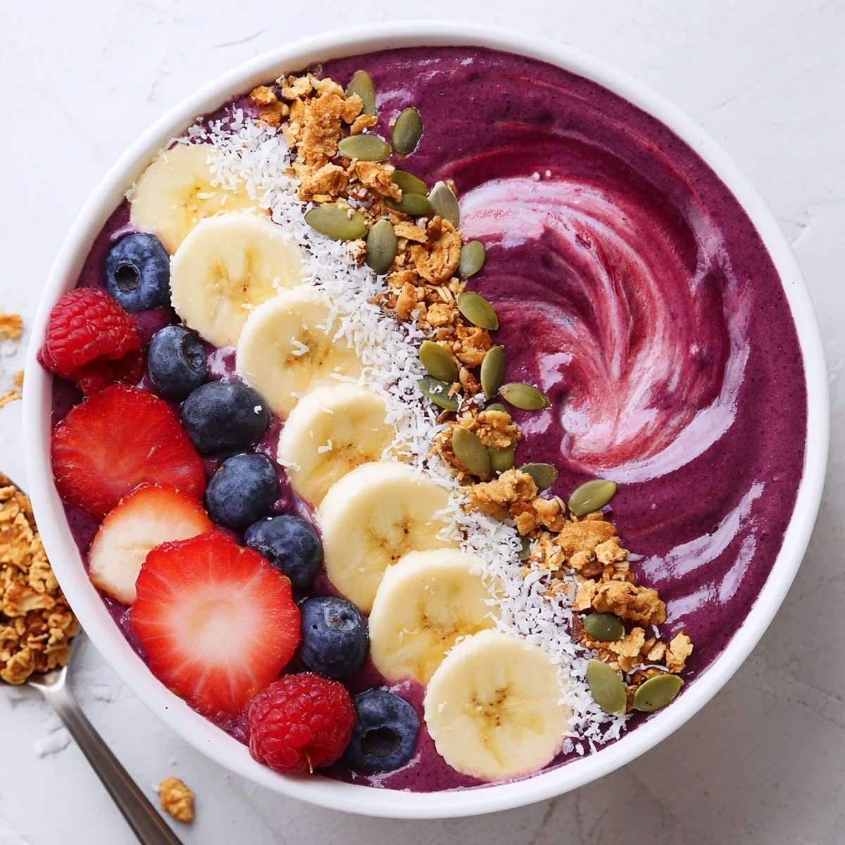 A thick, purple acai berry smoothie bowl with crunchy granola and pumpkin seeds for an energizing breakfast.