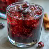 A close-up of deep ruby Black Currant Rum Liqueur poured into a chilled glass, glistening beside fresh blackcurrants and a vanilla bean.