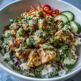 A vibrant Bang Bang Chicken Bowl with saucy chicken, crunchy carrots, and fresh cucumber over fluffy rice, drizzled with creamy spicy sauce.