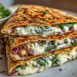 Cut wedge of a Mediterranean quesadilla showing red onion and melted cheese against a rustic wooden background.
