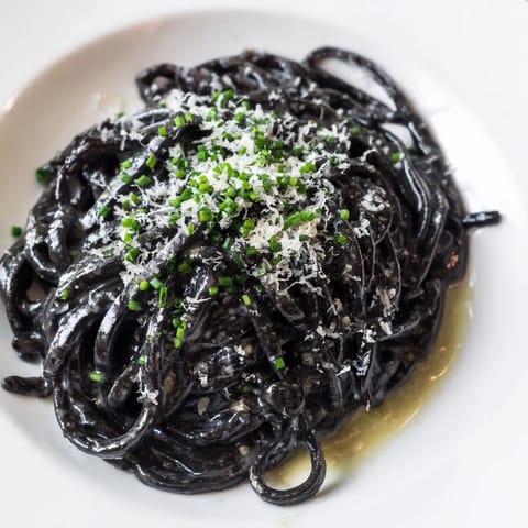 Dark, silky strands of squid ink pasta coated in a luscious cream sauce, garnished with lemon wedges.