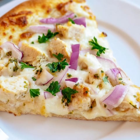 A slice of Chicken Alfredo Pizza with a crispy crust, garnished with fresh parsley and served beside a glass of Chardonnay.