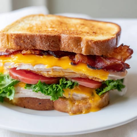 Toasted turkey club grilled cheese sandwich with melted cheddar, crispy bacon, and ripe tomato slices on buttery sourdough.