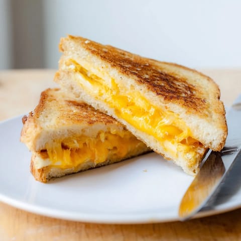 Toasted Triple Cheese Sourdough Grilled Cheese, cut diagonally and served beside a bowl of creamy tomato soup.