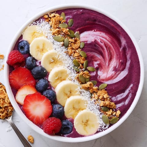A thick, purple acai berry smoothie bowl with crunchy granola and pumpkin seeds for an energizing breakfast.