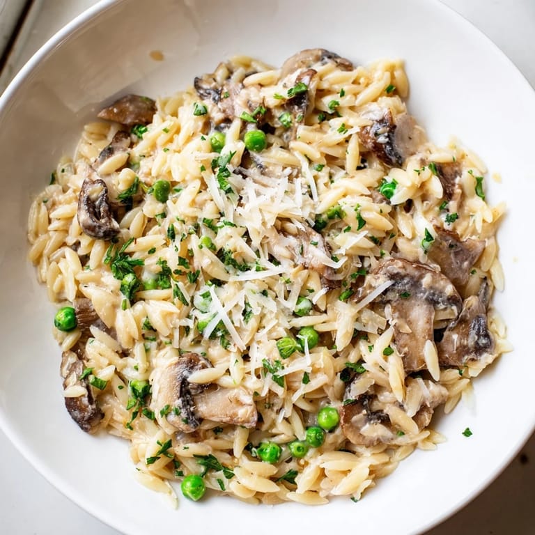Golden, cheesy Orzo Mushroom Risotto-Style in a skillet, garnished with fresh herbs and a sprinkle of black pepper.