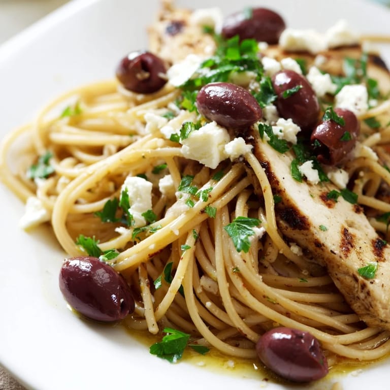 Freshly prepared Greek Chicken Spaghetti featuring briny Kalamata olives, parsley, and a drizzle of extra-virgin olive oil on a wooden table.