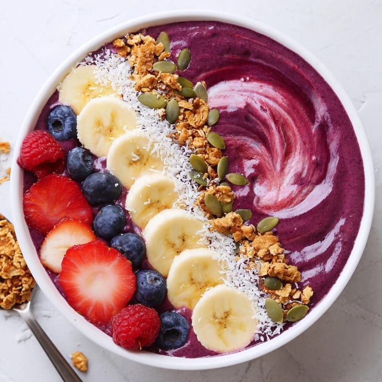 A thick, purple acai berry smoothie bowl with crunchy granola and pumpkin seeds for an energizing breakfast.